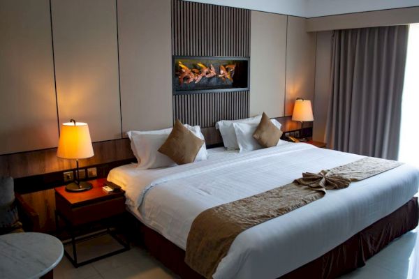 Hotel room with a large bed, decorative pillows, wall art, bedside lamps, and curtains. Cozy and neatly arranged, inviting atmosphere.