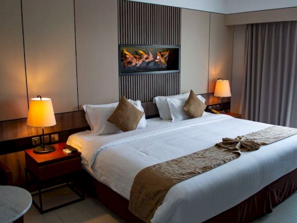 Hotel room with a large bed, decorative pillows, wall art, bedside lamps, and curtains. Cozy and neatly arranged, inviting atmosphere.