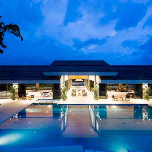 An elegant building with a large, illuminated pool in front, set against a vivid evening sky in a tranquil setting.