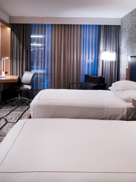 A modern hotel room with two beds, a wall-mounted TV, desk area, patterned carpet, and decorative wall, creating a cozy atmosphere.