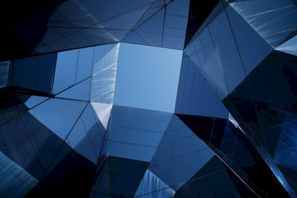 Glass and steel structures create a geometric pattern, leading the eye to a blue sky at the center, resembling modern architectural design.