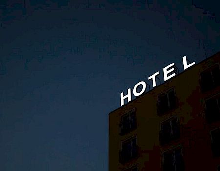 The image shows a building with a lit "HOTEL" sign against a dark evening sky.