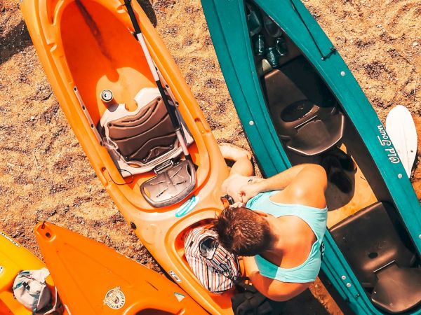 The image shows a person near colorful kayaks on a sandy surface, preparing or organizing equipment.