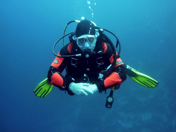 A scuba diver is underwater, wearing a wetsuit, mask, and fins, with a tank on their back, surrounded by blue water.