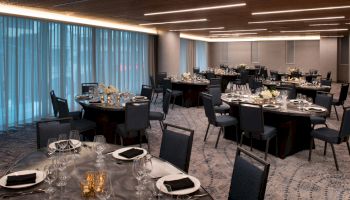 The image shows a banquet hall with round tables set for a formal event, featuring elegant table settings and modern decor.