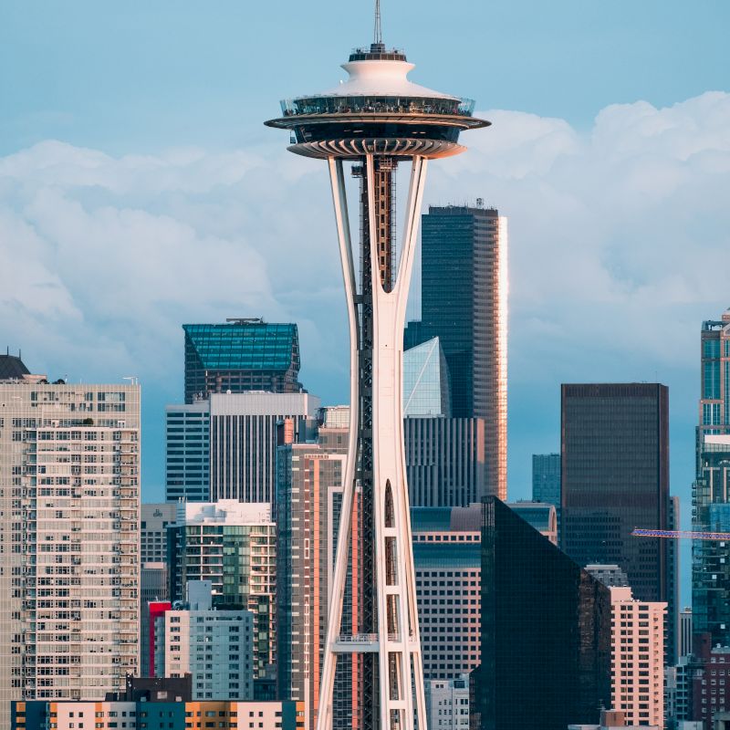 The image shows a cityscape with a prominent tower featuring a unique design, surrounded by various skyscrapers and buildings.