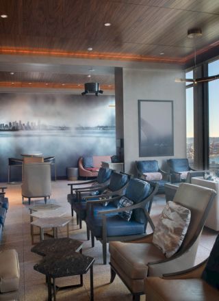 A modern lounge with comfortable chairs, large windows offering ocean views, and a mural depicting a cityscape on the back wall.