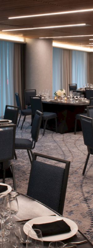 The image shows an elegantly set banquet hall with round tables, chairs, glassware, and decorative centerpieces under soft lighting.