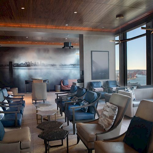 A modern lounge with elegant seating, a cityscape mural, and large windows offering a scenic water view and Ferris wheel in the distance.