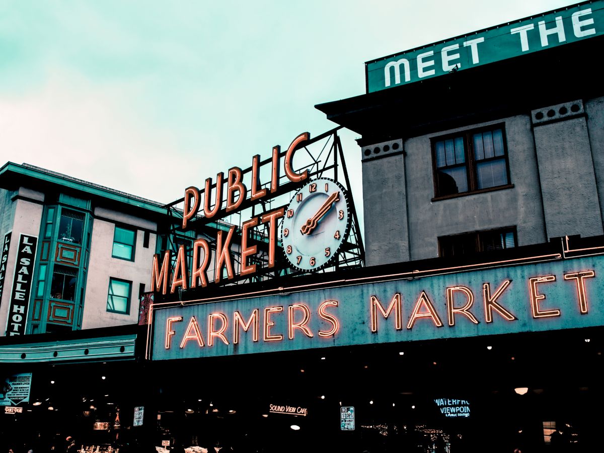 The image shows a famous market with neon signs reading "Public Market" and "Farmers Market," along with a clock above.