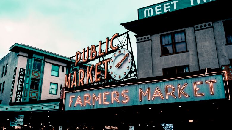 The image shows a famous market with neon signs reading "Public Market" and "Farmers Market," along with a clock above.