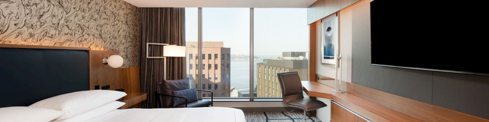 A modern hotel room with a large bed, desk, chair, wall-mounted TV, and window offering a city view ends the sentence.